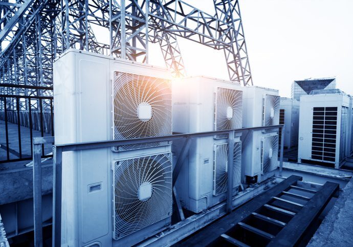 Air conditioner units (HVAC) on a roof of industrial building with blue sky and clouds in the background.